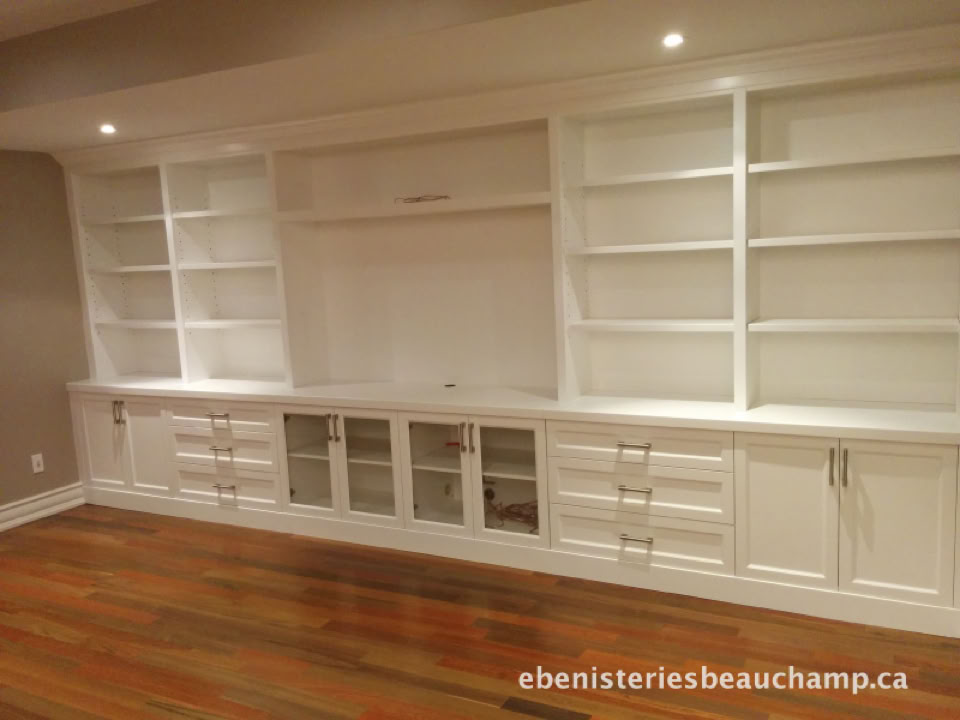 White built-in shelving unit with cabinets and open shelves, set against a wall with wooden flooring.