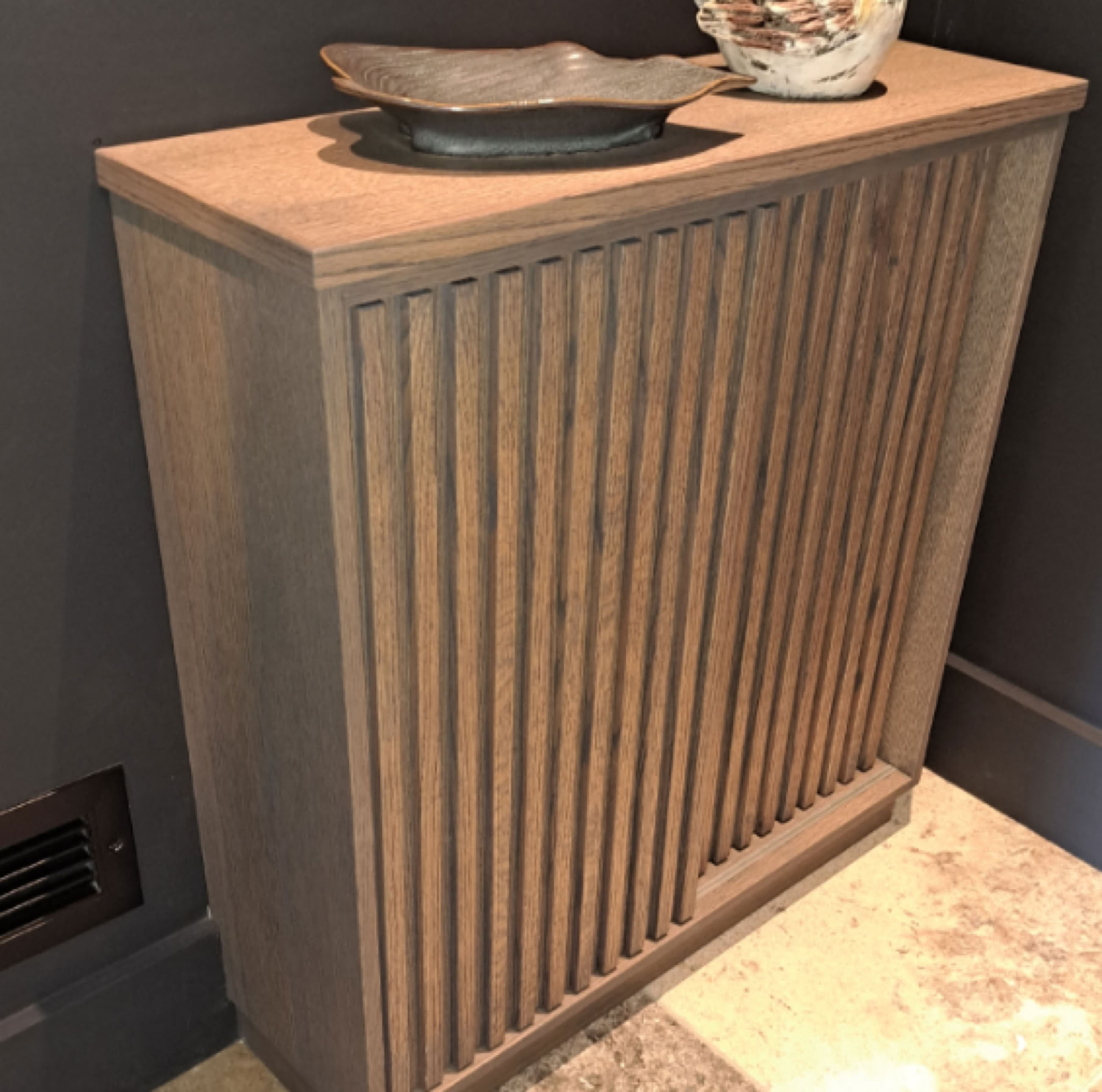 Meuble en bois avec des rainures verticales, surmonté de deux objets décoratifs.