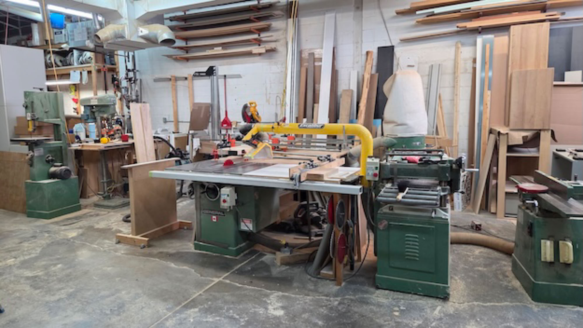 Atelier de menuiserie avec des machines, des outils et des planches de bois empilées contre le mur.