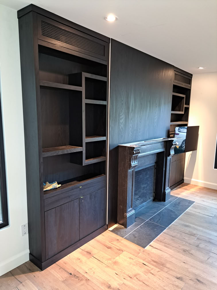 Dark wooden built-in shelves and a fireplace with a mantel, set against a light-colored wall and hardwood floor.